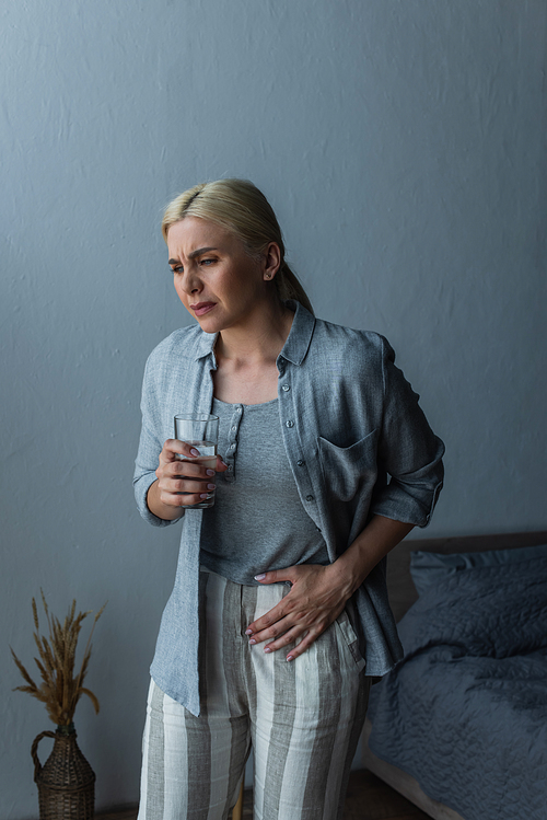woman with menopause holding glass of water while suffering from abdominal pain