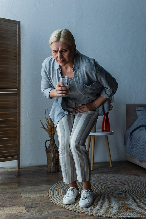 stressed woman with menopause holding glass of water while suffering from abdominal pain