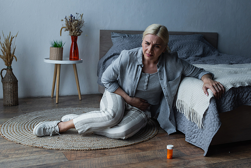woman with menopause sitting near bed while suffering from abdominal pain