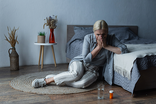 woman with menopause sitting near bed while covering face and suffering from abdominal pain