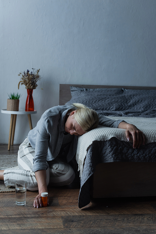 exhausted woman having menopause and holding bottle with painkillers while suffering from pain