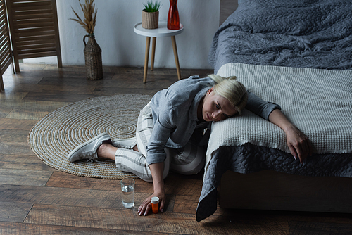 stressed woman having menopause and holding bottle with painkillers while suffering from pain in bedroom