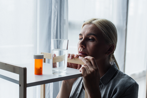 blonde woman with menopause looking at medication and glass of water on table