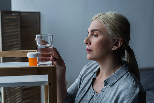 blonde woman with menopause looking at medication and reaching glass of water on table