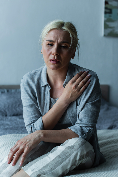 exhausted blonde woman sitting in bedroom during menopause