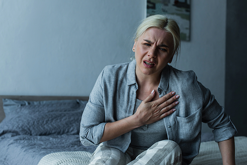 exhausted blonde woman touching chest and feeling pain during menopause