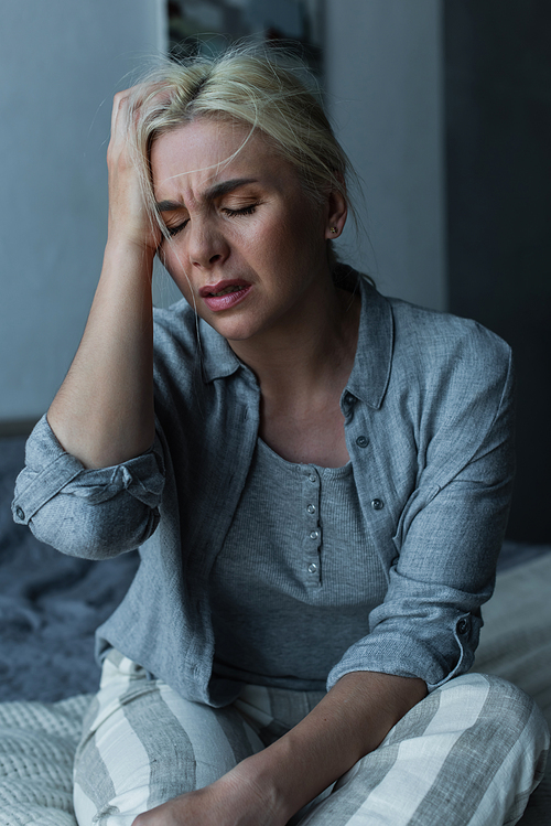 exhausted blonde woman touching head and having migraine during menopause