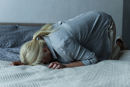 blonde woman lying on bed while feeling pain in stomach during menopause