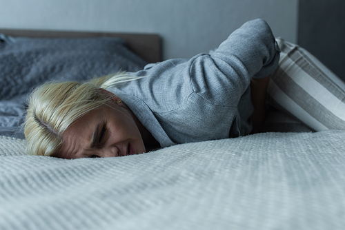 stressed woman lying on bed while feeling pain in stomach during menopause