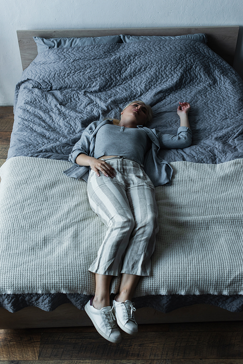 high angle view of blonde woman lying on bed while feeling pain in stomach during menopause