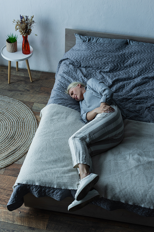 high angle view of blonde woman lying on bed while having stomach ache during menopause