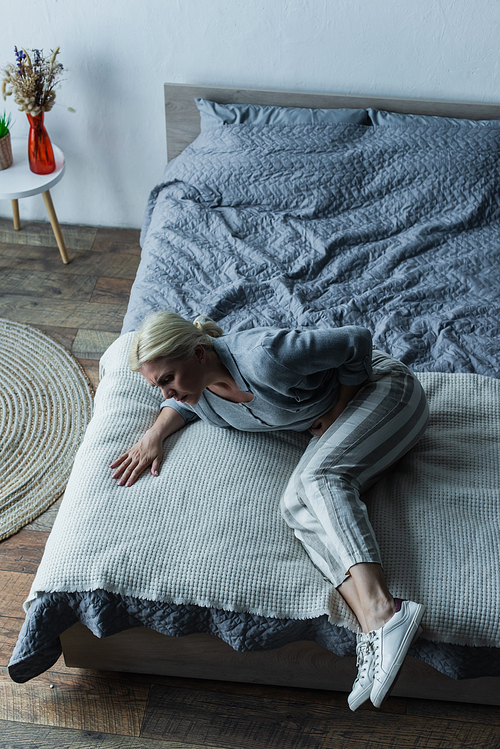 high angle view of frustrated woman lying on bed while feeling pain in stomach during menopause