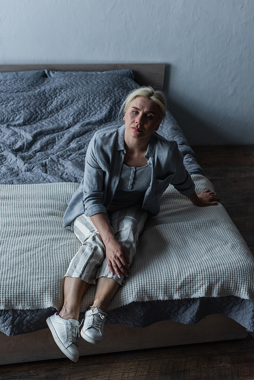 high angle view blonde woman sitting on bed while feeling pain in stomach during menopause