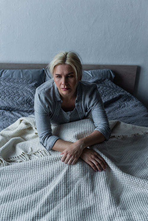 blonde and depressed woman with blue eyes feeling unwell during menopause while sitting in bed