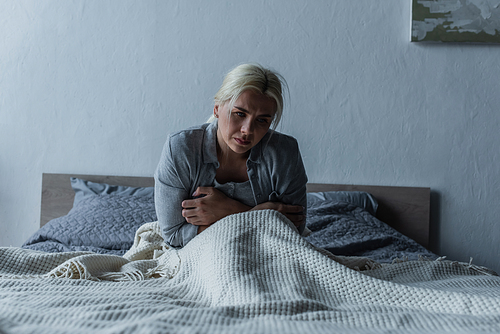 depressed woman with blue eyes feeling unwell during menopause while sitting in bed