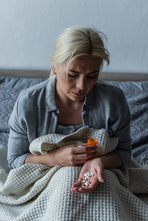 sad woman with climax sitting in bed and looking at bottle with painkillers