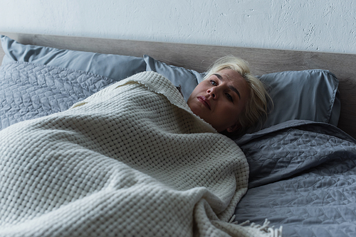 depressed blonde woman with menopause lying under blanket in bed