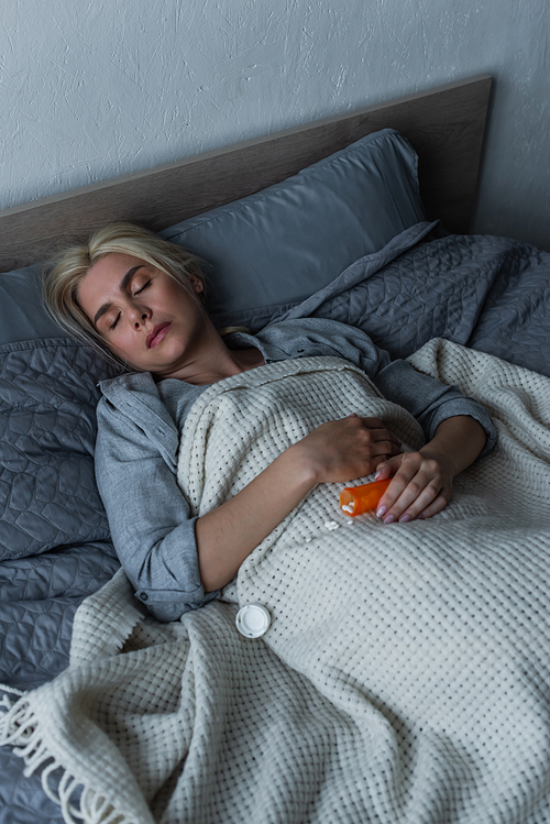 high angle view of depressed blonde woman with menopause sleeping near pills in bed