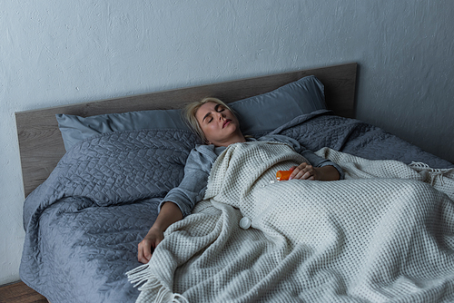 depressed blonde woman with menopause sleeping near pills in bed
