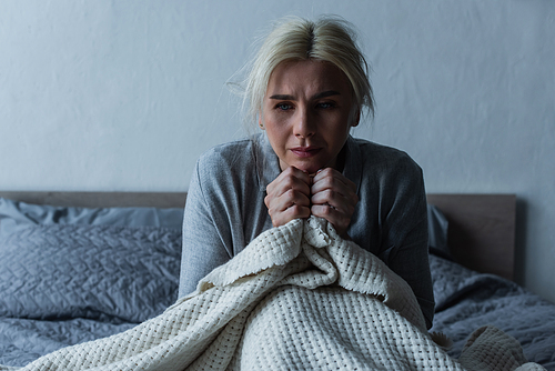 depressed blonde woman with menopause holding blanket while in bed