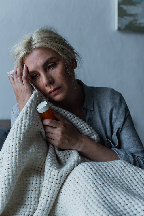 depressed blonde woman with menopause holding bottle with sleeping pills in bed