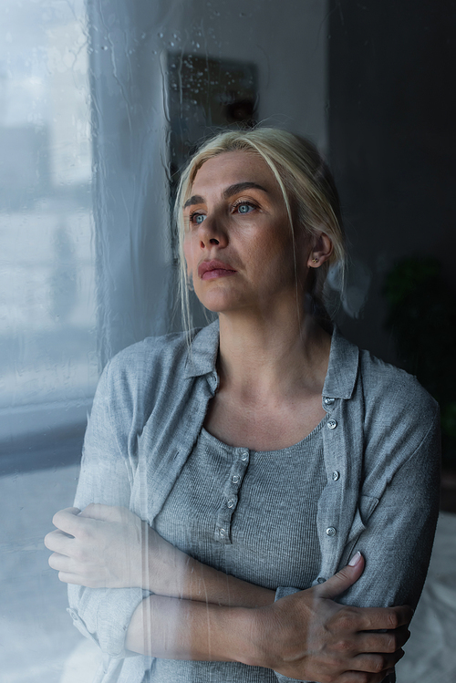 depressed blonde woman looking at window with rain drops