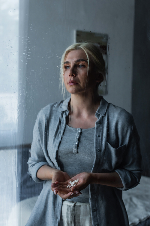 depressed blonde woman pills and looking at window with rain drops