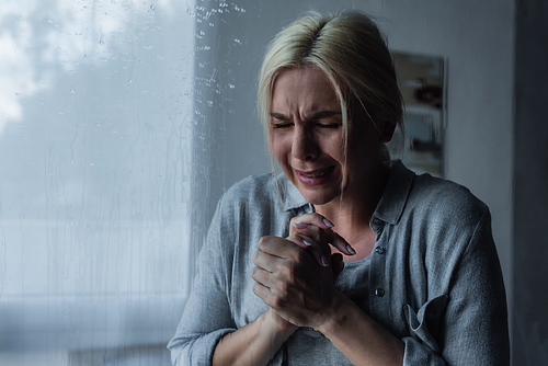 depressed blonde woman crying behind window glass with rain drops