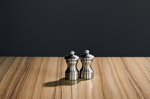 metal salt and pepper shakers on wooden table isolated on black