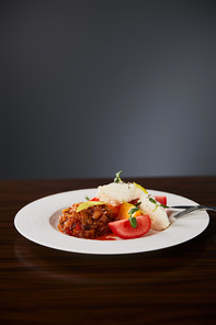 delicious restaurant dish with eggplant caviar and tomatoes served on wooden table with cutlery on black background