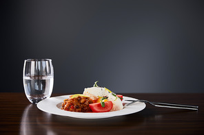 delicious restaurant dish with eggplant caviar and tomatoes served on wooden table with water and cutlery on black background