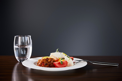 delicious restaurant dish with eggplant caviar and tomatoes served on wooden table with water and cutlery on black background