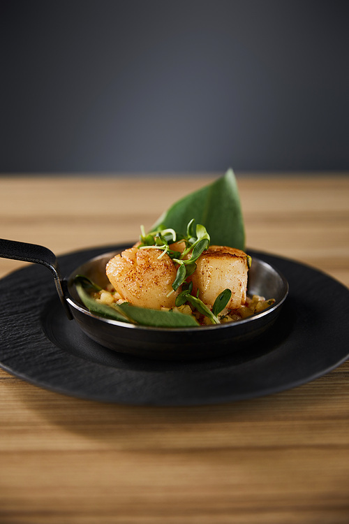 delicious grilled scallops with green leaves and microgreens on wooden table on black background