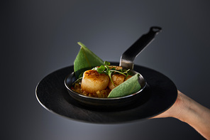 cropped view of woman holding plate with delicious grilled scallops on black background