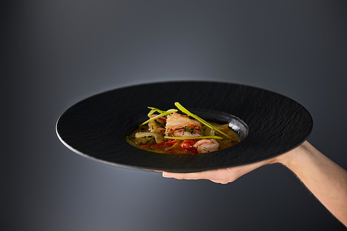 cropped view of woman holding plate with shrimp soup on black background