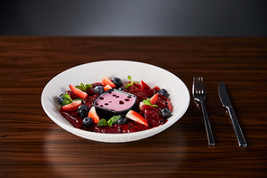 selective focus of traditional Ukrainian varenyky with berries served in white plate with sauce near cutlery on wooden table