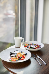 traditional Ukrainian varenyky and syrniki with berries served in white plate with sauce near cutlery and cup on wooden table in restaurant