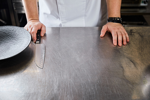 cropped view of chef standing at metal surface at kitchen in restaurant