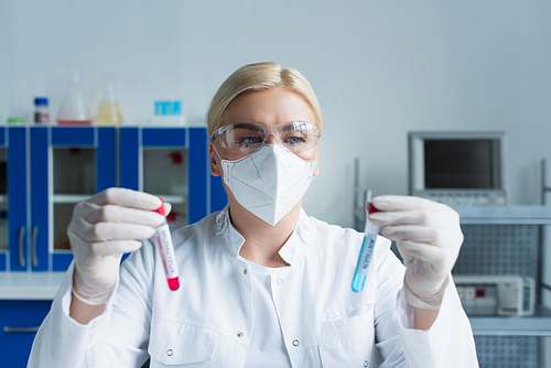 Scientist in protective mask holding blurred test tubes in laboratory