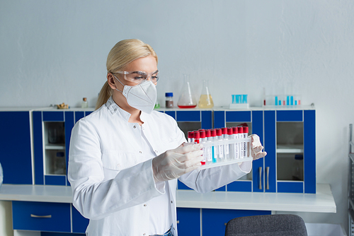 Scientist in latex gloves and protective mask holding test tubes in laboratory