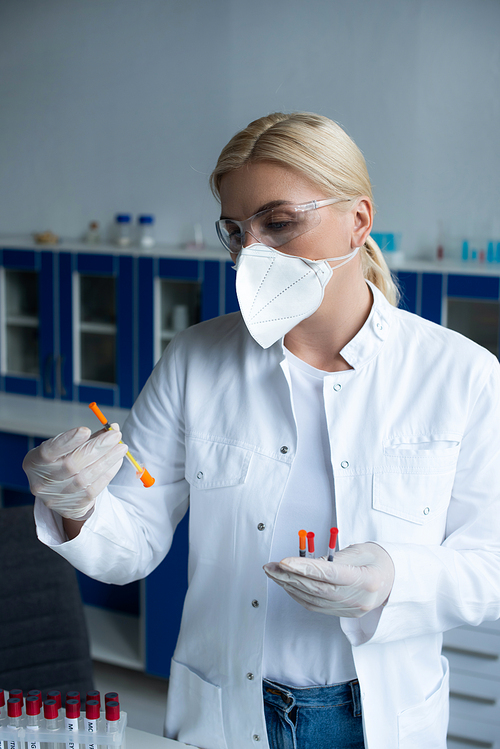 Scientist in protective goggles holding syringes near test tubes in lab