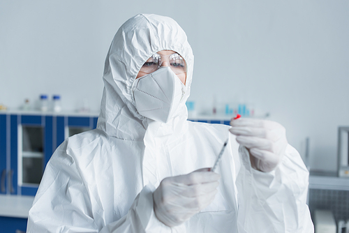 Scientist in hazmat suit and goggles holding syringe in laboratory