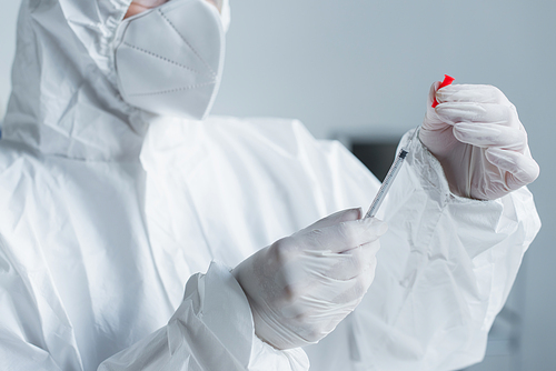 Cropped view of scientist in hazmat suit in latex gloves holding syringe in lab
