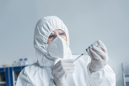 Scientist in protective suit and goggles holding syringe and vaccine in lab