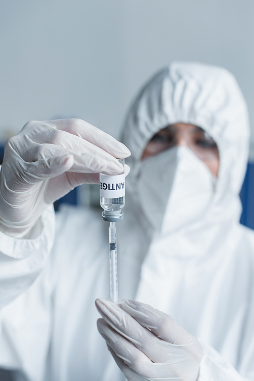Blurred scientist in latex gloves holding antigen and syringe in laboratory