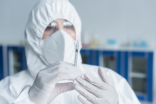 Blurred scientist in hazmat suit holding syringe in laboratory