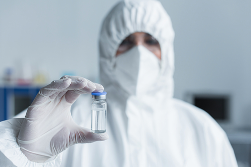 Blurred scientist in hazmat suit holding vaccine in lab