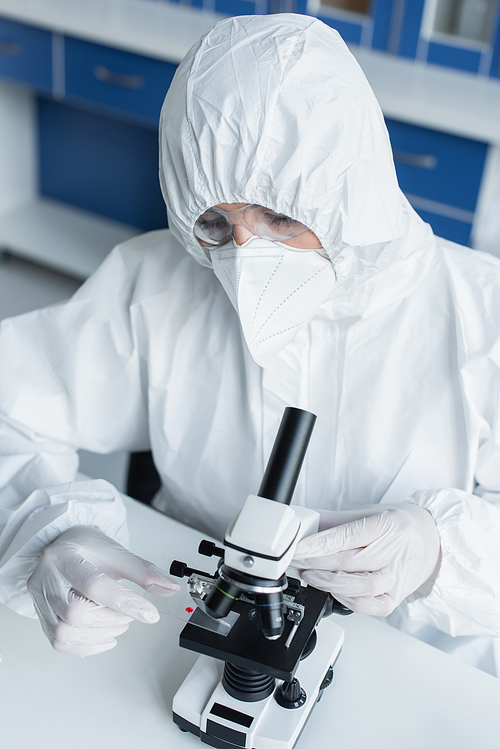 Scientist in hazmat suit holding glass near microscope in lab