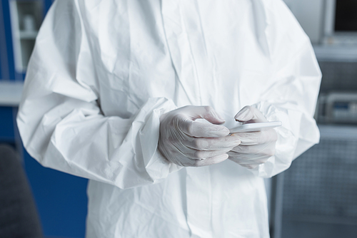 Cropped view of scientist in protective suit and latex gloves using mobile phone in lab