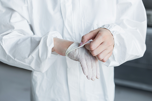 Cropped view of scientist in hazmat suit taking off latex glove in lab